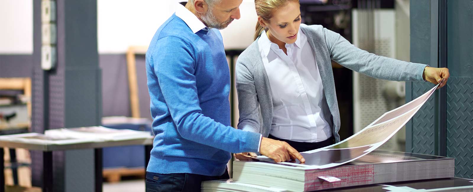 An older man in a blue shirt discusses a poster that a woman in a grey shirt is holding and looking at.